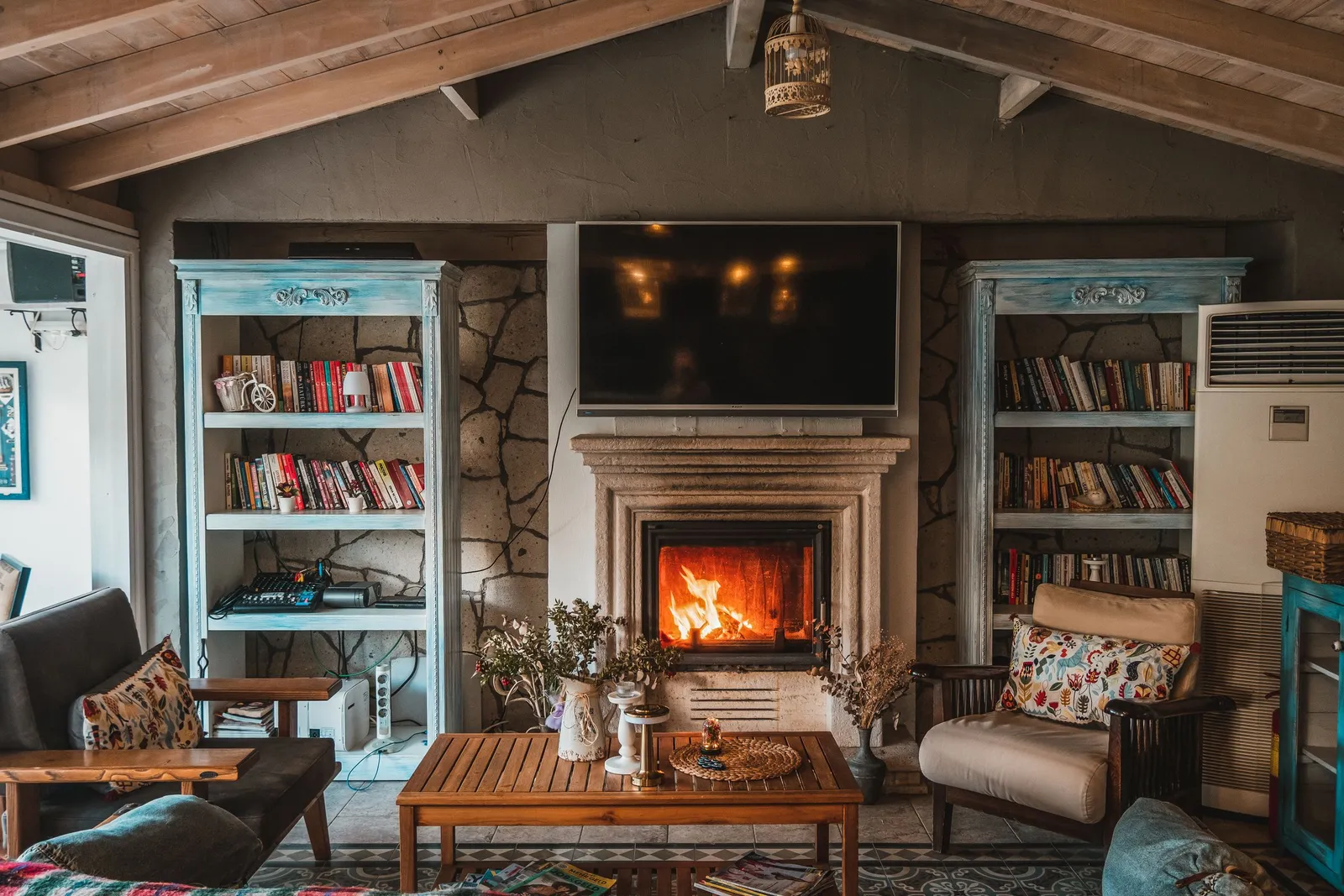 Finished family room with a lit stone fireplace, built-in bookshelves and a wood-beam ceiling