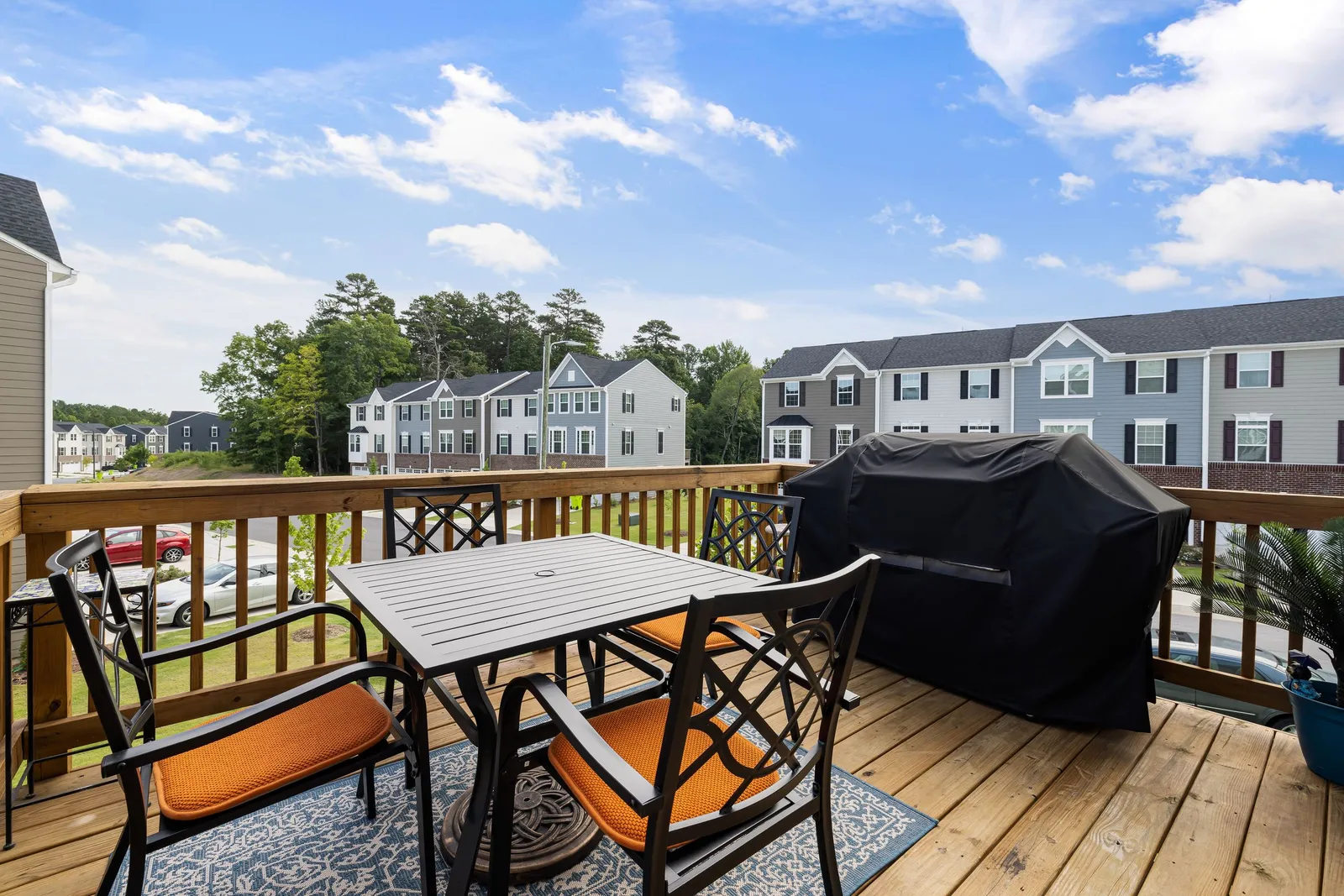 Wood deck with railing, a patio table and chairs, and a covered grill