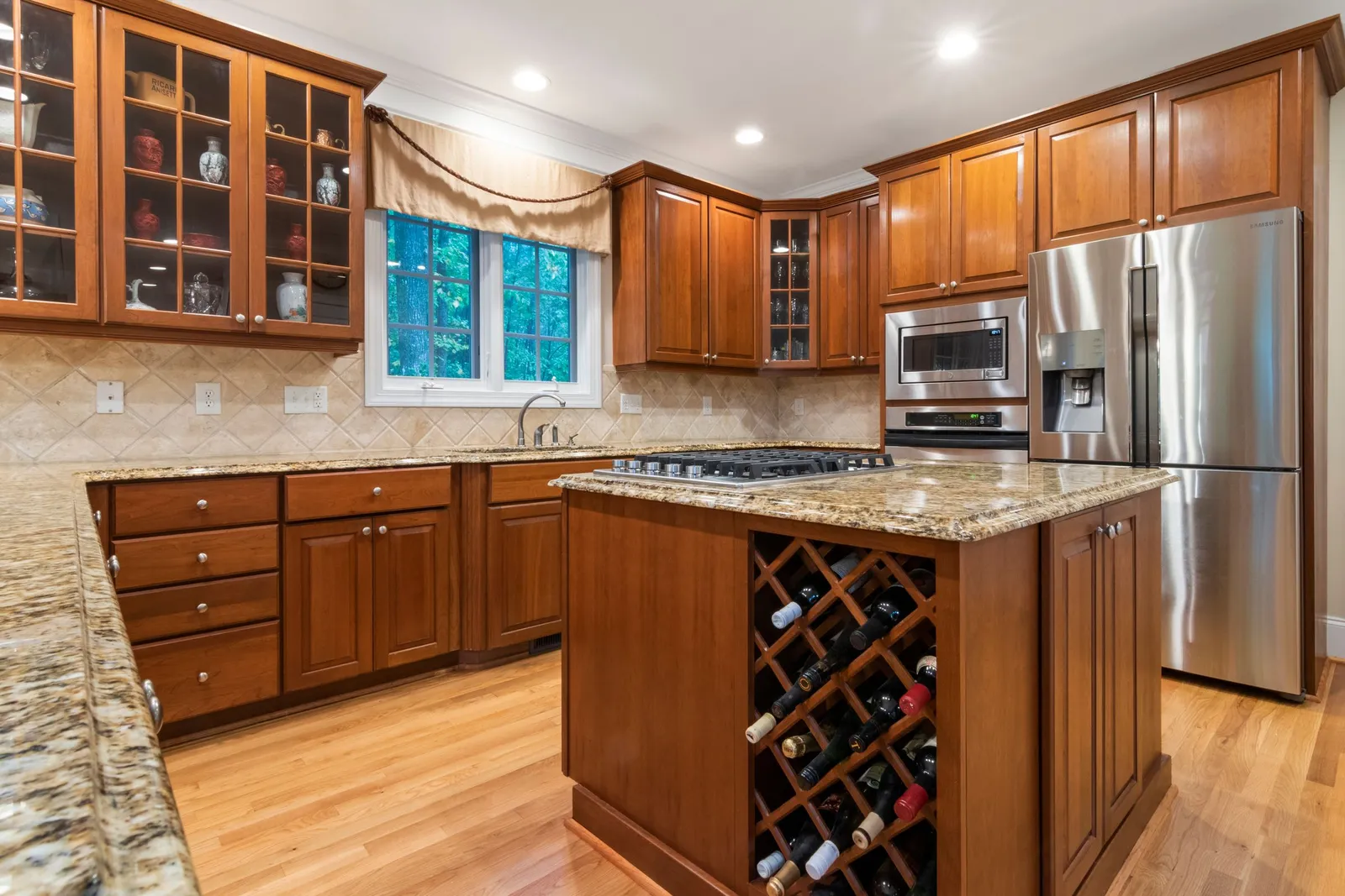 Stained wood cabinetry with glass-front doors, crown molding and a built-in wine rack in the island