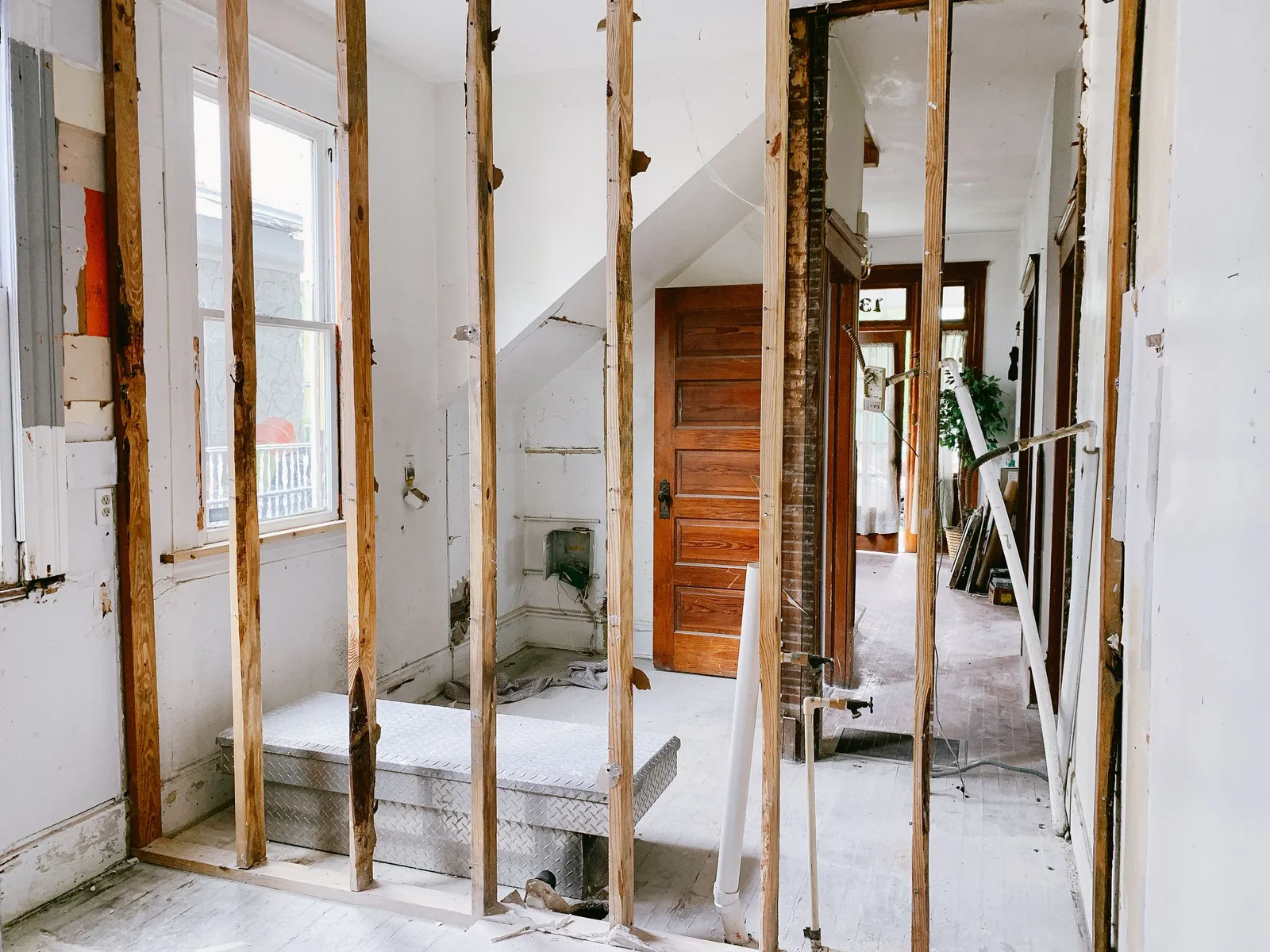 Gutted interior mid-renovation with exposed stud walls, a bare doorway and a staircase beyond