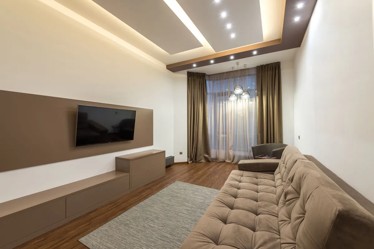Media room with a wall-mounted television, a tan sectional and recessed cove lighting