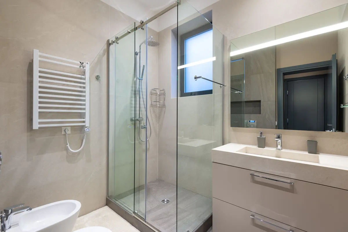 Walk-in shower with a sliding glass door next to a wall-hung vanity and towel warmer