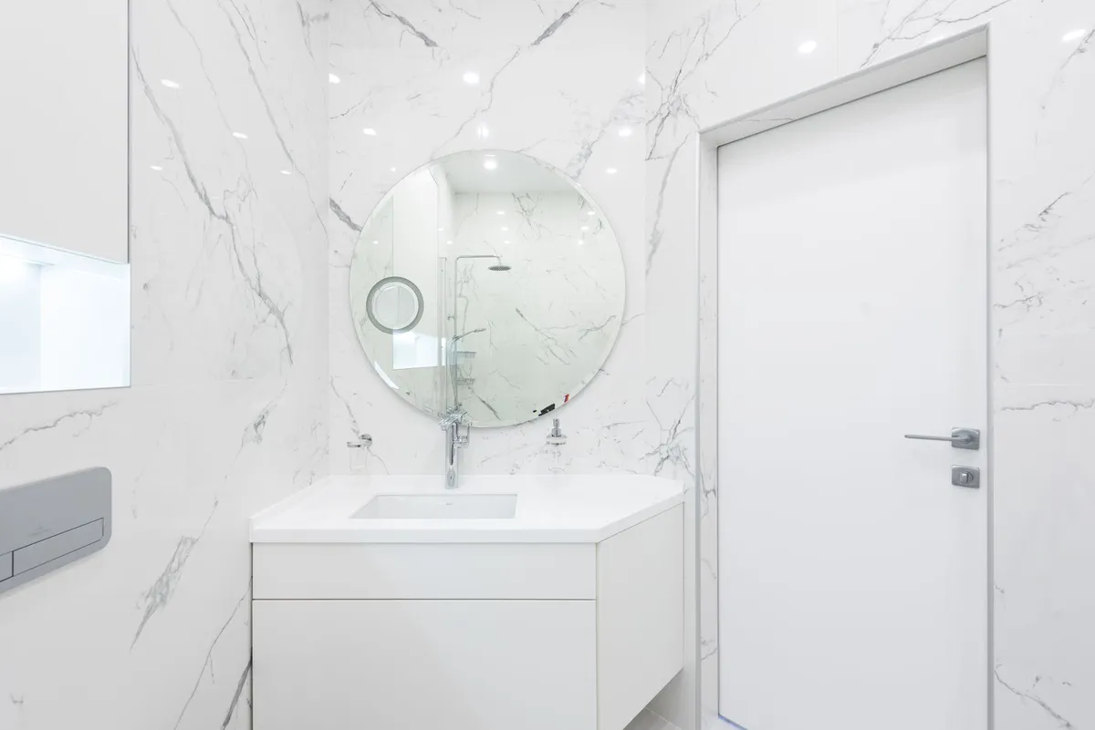 Floating vanity with an undermount sink and a round mirror against marble-look wall tile
