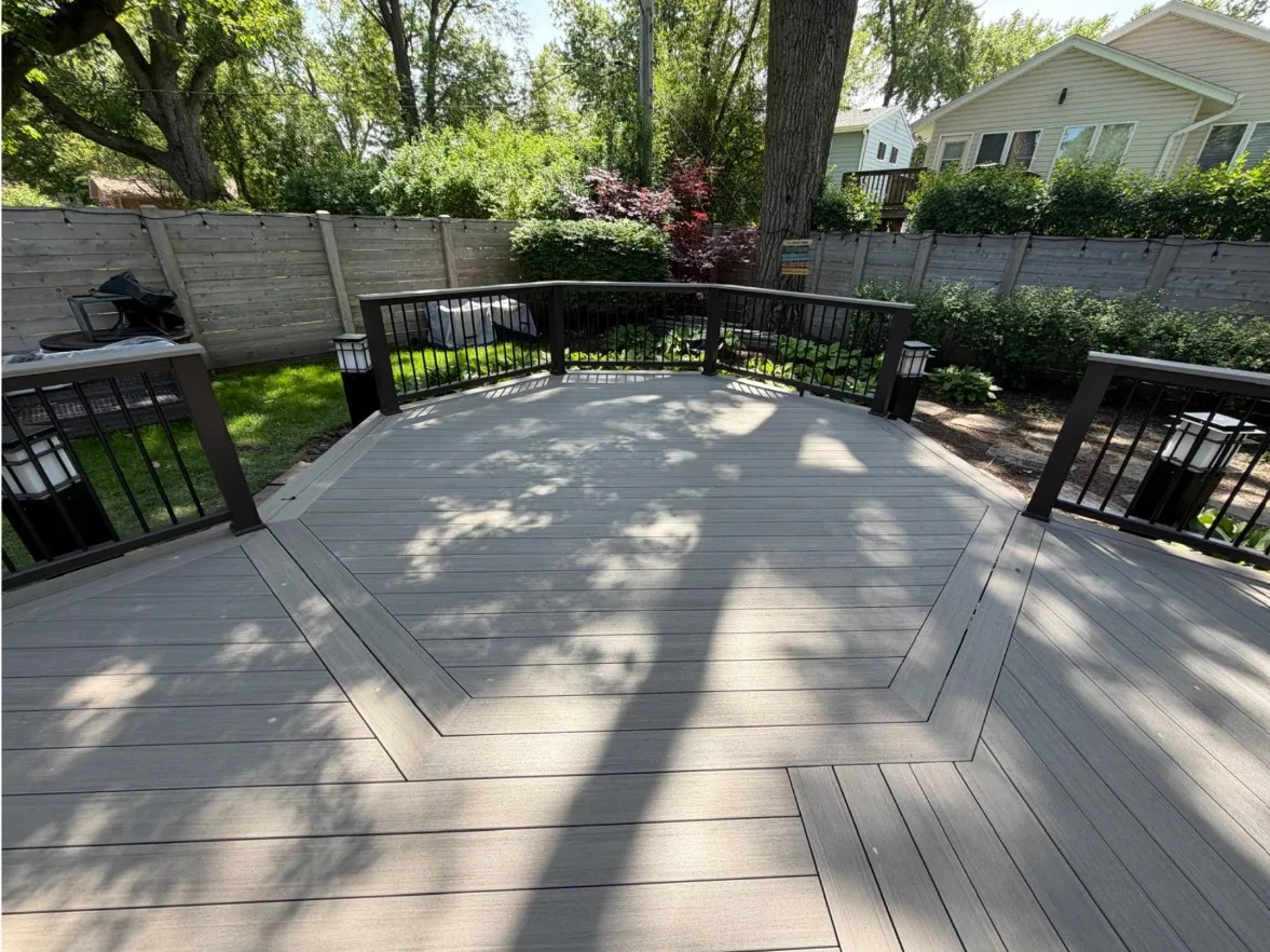 Composite deck boards laid inside a mitered picture-frame border, with black aluminum balusters and lit post caps