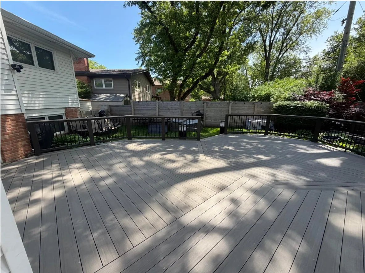 Wide gray composite deck with black metal railing at the back of a house, enclosed by a wood privacy fence