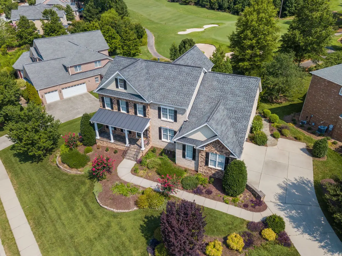 Aerial view of a two-story home with a shingled roof, landscaped beds and a paved driveway