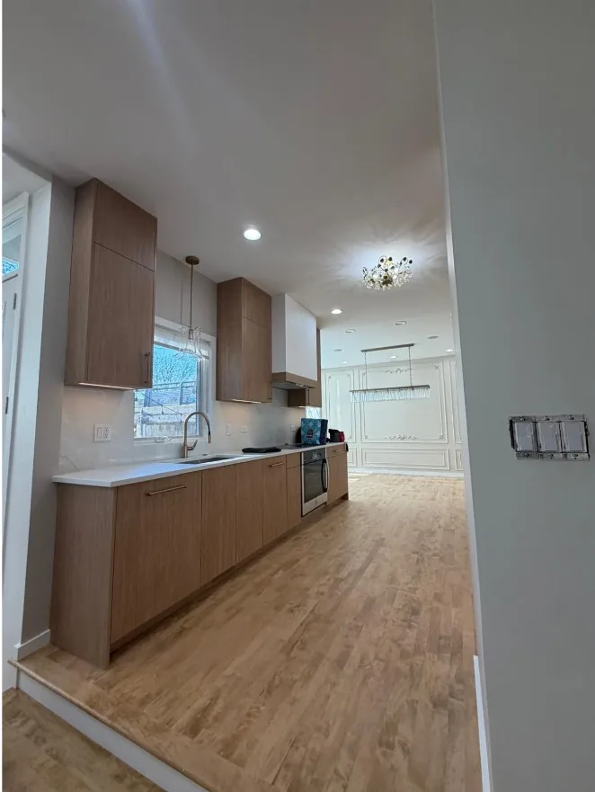 Single-wall kitchen run with light wood cabinets, a white quartz countertop and backsplash, a wall oven and pendant lights over the sink