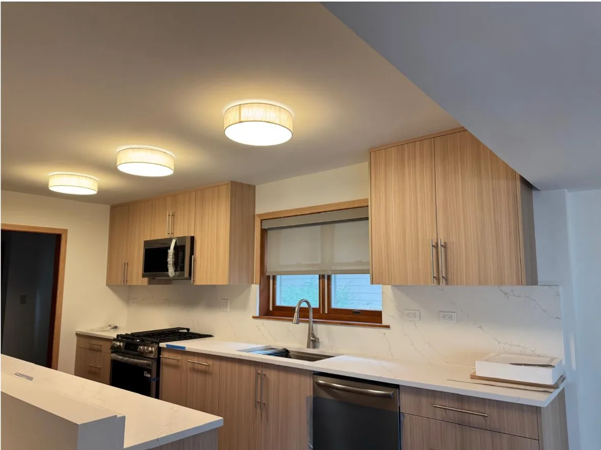 Kitchen with light oak flat-panel cabinets, white quartz countertops and a matching quartz backsplash, a stainless gas range and three drum ceiling lights