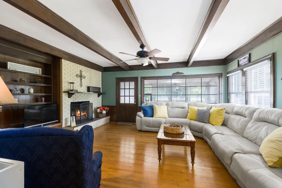 Living room with exposed ceiling beams, a stone fireplace and a large sectional on hardwood floors