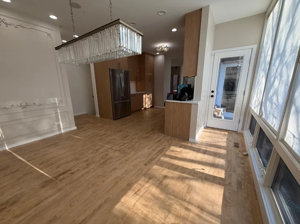 Open living and dining space with light hardwood flooring running through to a wood-cabinet kitchen beyond