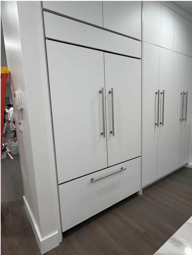 Floor-to-ceiling white cabinetry with a panel-front refrigerator and long stainless bar pulls, over wide-plank wood flooring