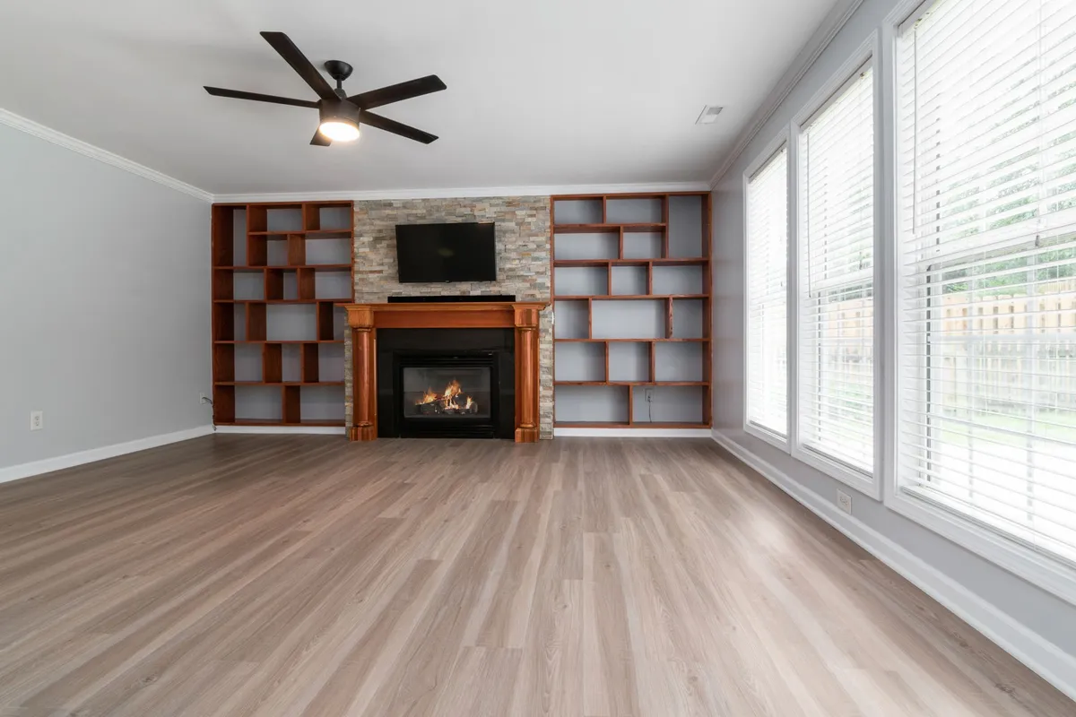 Built-in wood shelving flanking a fireplace in an empty room with wide-plank flooring
